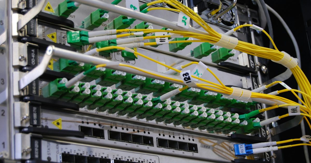 Yellow fiber optic cables plugged into green ports on a silver network switch in a rack