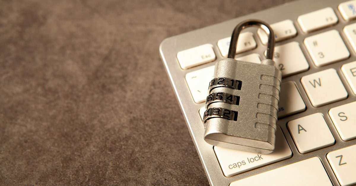 Silver combination padlock resting on the corner of a white computer keyboard on a brown desk surface.